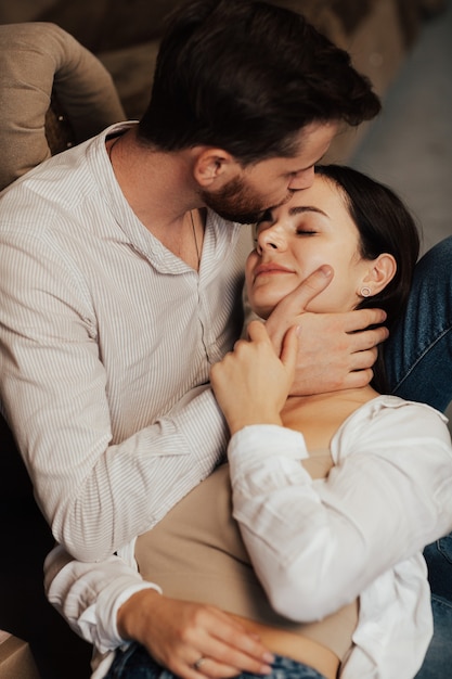 Homme barbu embrassant sa femme sur le front alors qu'elle sourit les yeux fermés.