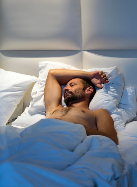 Homme barbu endormi allongé dans son lit sur le dos sous une couverture blanche Homme nu endormi pose les yeux fermés Portrait à la taille d'un bel homme caucasien musclé nu dort dans la chambre