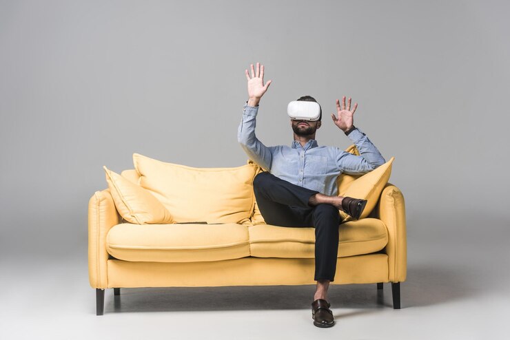 Photo homme barbu faisant des gestes et utilisant un casque de réalité virtuelle et assis sur un canapé jaune sur gris
