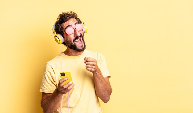 Homme barbu fou expressif écoutant de la musique avec des écouteurs et un sartphone