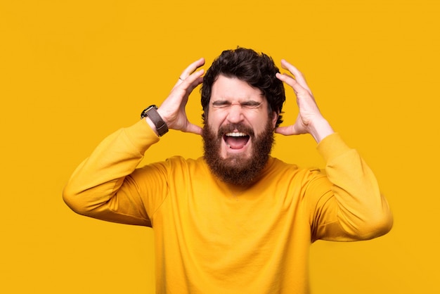 Un homme barbu frustré crie ou crie les yeux fermés et les mains près de la tête.