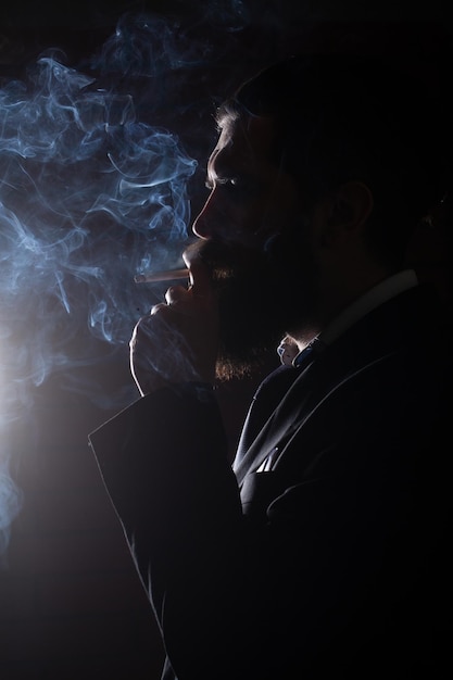 Homme barbu fumant de la fumée de cigarette sur fond noir