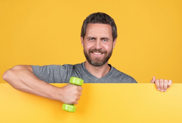 Un homme barbu heureux derrière du papier jaune tient un outil d'haltères de remise en forme pour l'entraînement sur place, la publicité.