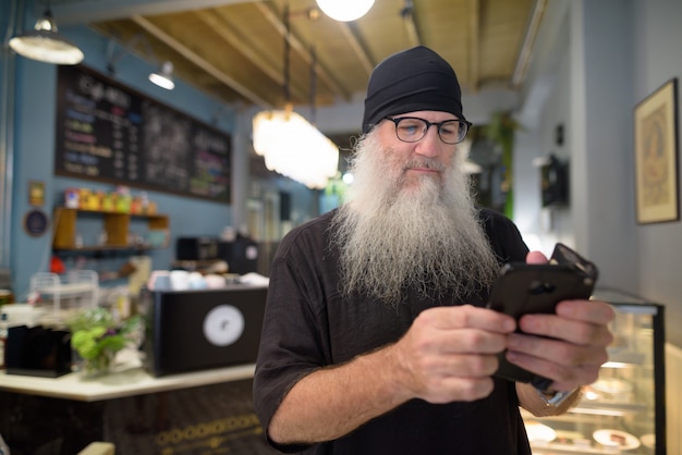 Homme barbu hipster mature à l'aide de téléphone avec des lunettes au café