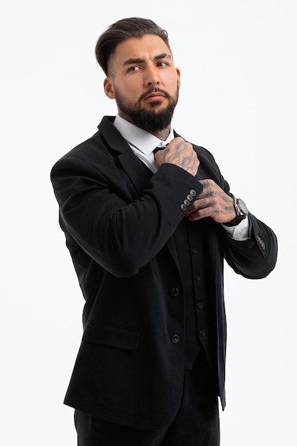 Homme barbu hispanique confiant avec les mains tatouées en chemise blanche et pantalon noir ajustant la cravate