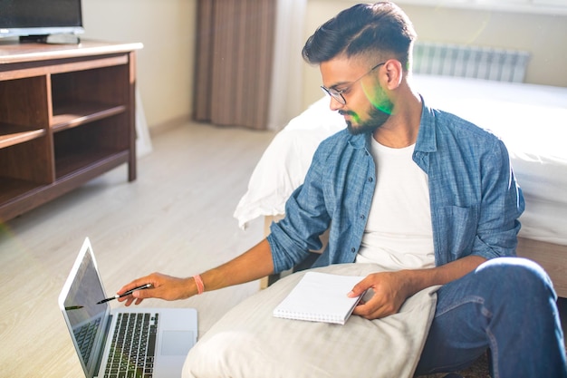 Homme barbu indien assis sur le sol et faisant des calculs financiers en ligne dans un nouvel appartement