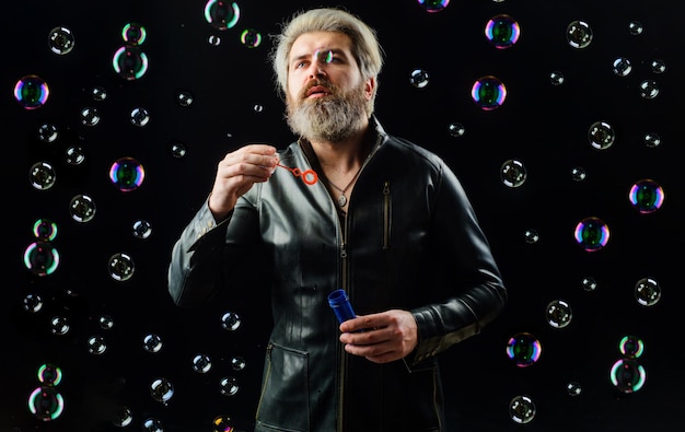 Photo homme barbu jouer avec des bulles de savon bonheur enfance mec en veste de cuir soufflant bulle