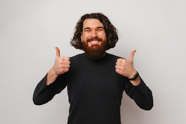 Un homme barbu joyeux aux cheveux longs montre et tient deux pouces vers le haut