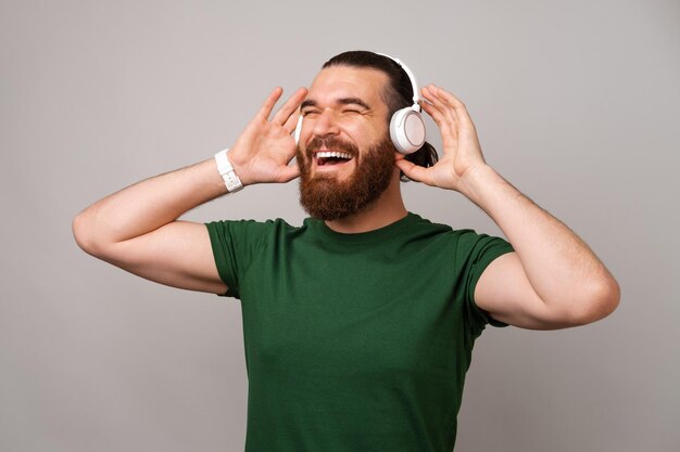 Un homme barbu joyeux portant un t-shirt vert portant des écouteurs s'amuse