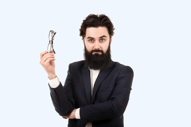 Homme barbu avec des lunettes pour vue dans la main, image sur un mur bleu