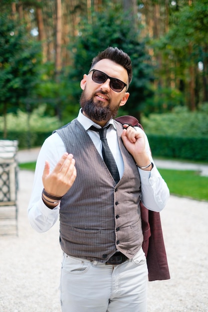 Homme barbu en lunettes de soleil et costume à l'extérieur