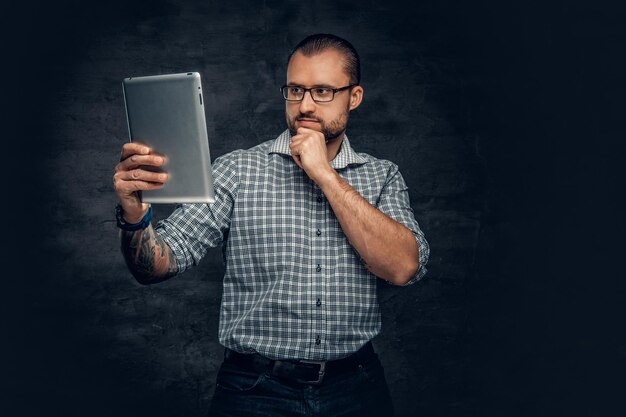 Un homme barbu en lunettes de soleil tient une tablette PC sur fond gris.