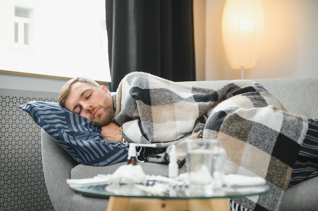 Homme barbu malade qui a un mauvais rhume ou une grippe saisonnière assis sur un canapé à la maison Un gars avec de la fièvre portant un plaid chaud frissonnant avec une expression de visage inquiet