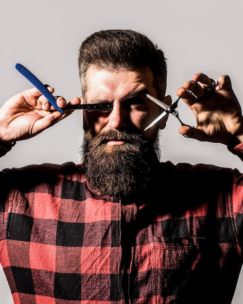 Homme barbu, mâle barbu. Portrait de barbe d'homme élégant. Ciseaux de coiffeur et rasoir droit, salon de coiffure. Salon de coiffure vintage, rasage