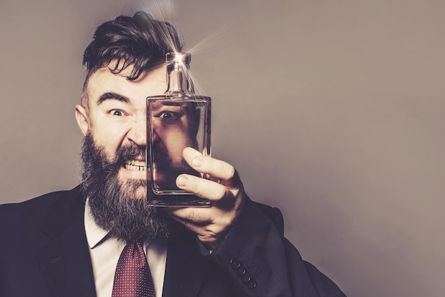 Homme barbu maléfique en costume regardant à travers une bouteille d'alcool