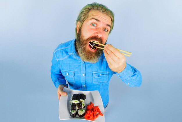 Homme barbu mangeant des sushis beau mec avec une assiette de rouleau de sushi et de la nourriture japonaise au gingembre mariné