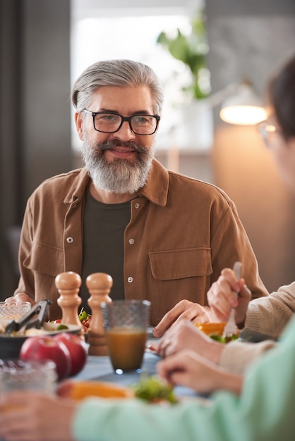 Homme barbu mature assis à table à manger pendant le déjeuner avec sa famille