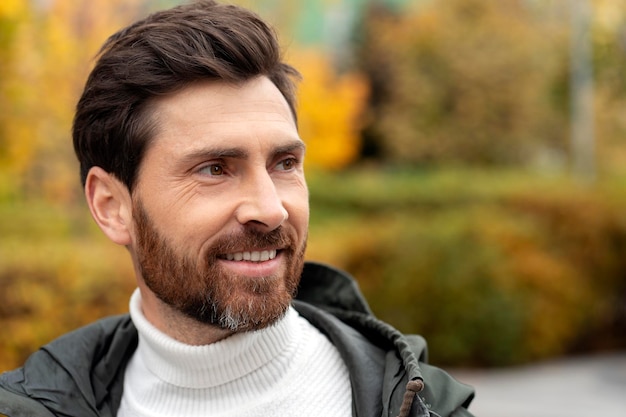 Homme barbu mature souriant à l'extérieur tout en regardant ailleurs