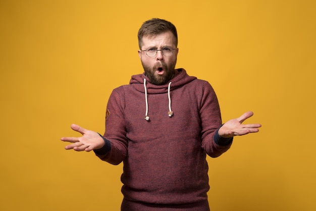 Un homme barbu mécontent et agacé avec des lunettes lève les mains dans la confusion et dit quelque chose