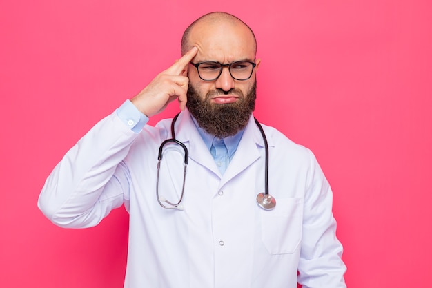 Homme barbu médecin en blouse blanche avec stéthoscope autour du cou portant des lunettes à côté confus pointant avec l'index sur sa tempe