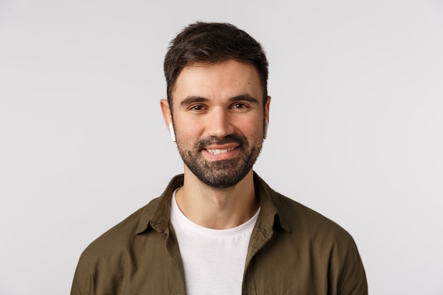 Homme barbu moderne vivant dans la ruée urbaine, portant des écouteurs sans fil écouter de la musique et souriant sans soucis, comme la qualité des écouteurs