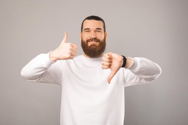 L'homme barbu montre des pouces vers le haut et vers le bas tourné en studio sur fond gris