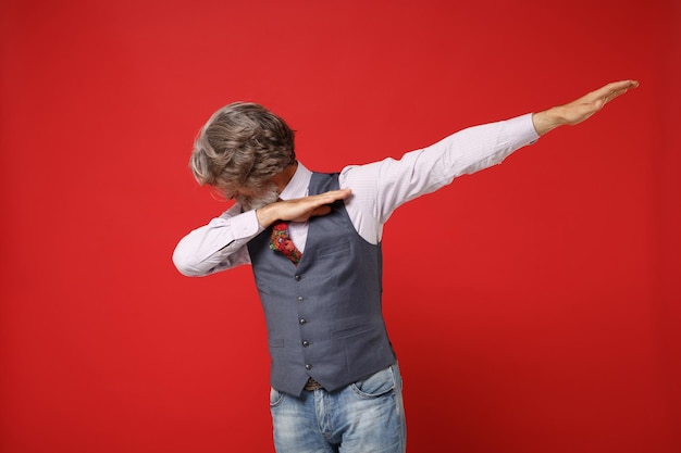 Homme barbu à moustache aux cheveux gris âgé en gilet de chemise classique et cravate colorée isolé sur fond rouge, portrait en studio. Concept de style de vie des gens. Maquette de l'espace de copie. Affichage du geste de danse DAB.