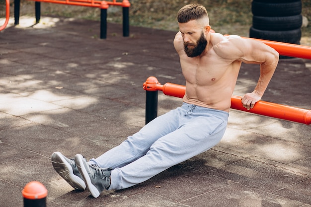 Homme barbu musclé fort faisant des pompes sur des barres inégales dans la salle de sport de rue en plein air. Concept de mode de vie d'entraînement.