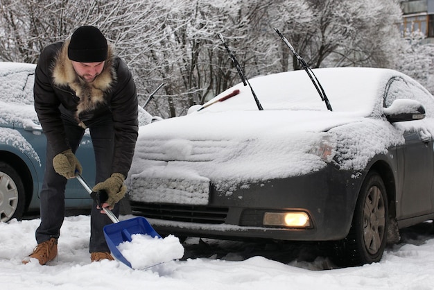 Un homme barbu nettoie la neige d'une voiture un matin d'hiver