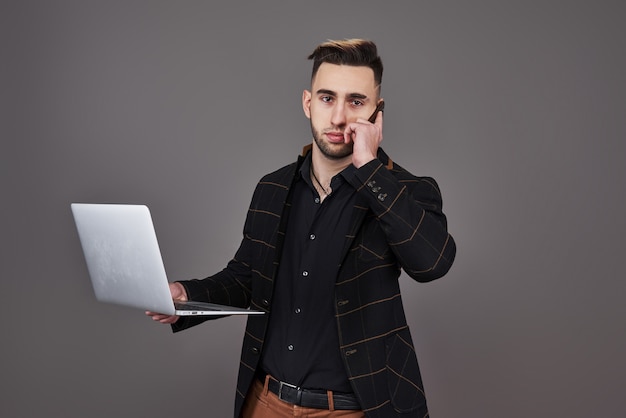 Homme barbu occupé en vêtements d'affaires, parler par smartphone et à l'aide d'un ordinateur portable