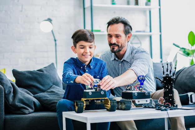 Homme barbu optimiste et son fils assis à la table tout en étant impliqués dans l'ingénierie robotique