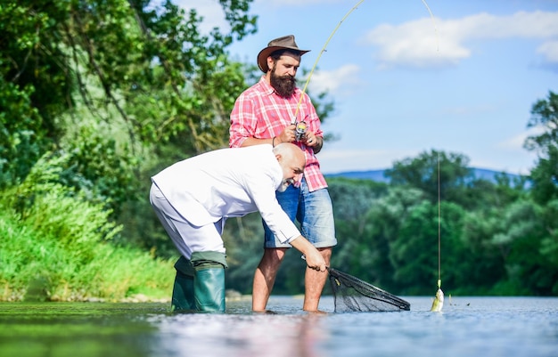 Homme barbu et pêche hipster brutale Équipe de pêche Journée active Journée familiale Passe-temps et loisirs Attraper du poisson avec l'âme sœur Amis attrapant du poisson Tranquillité d'esprit et tranquillité Poisson d'eau douce