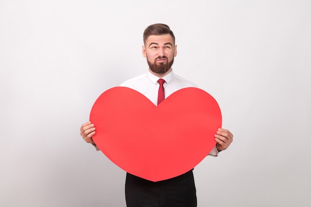 Homme barbu pensif tenant le coeur rouge et pensant à l'amour