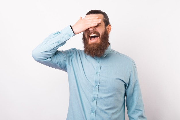 Un homme barbu portant une chemise fait un geste facepalm.