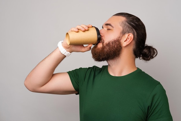Un homme barbu portant un t-shirt vert aime boire du café dans une tasse à emporter