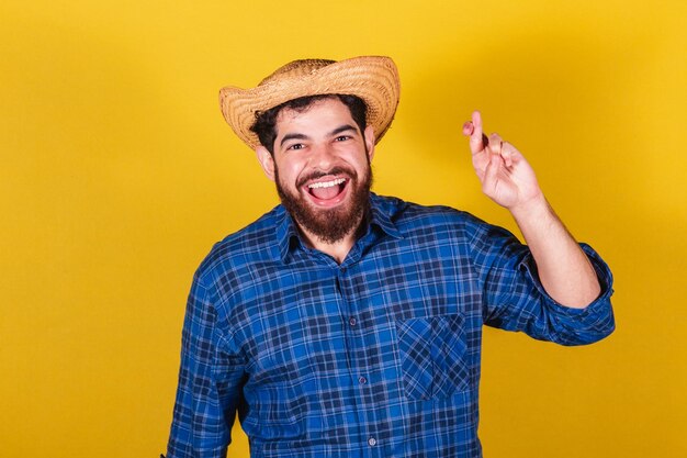 Homme barbu portant des vêtements typiques pour la Festa Junina Fête d'Arraia de Sao Joao Doigts croisés tordant plein d'espoir