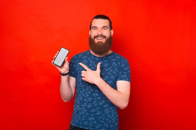 Un homme barbu positif présente quelque chose sur l'écran de son téléphone.