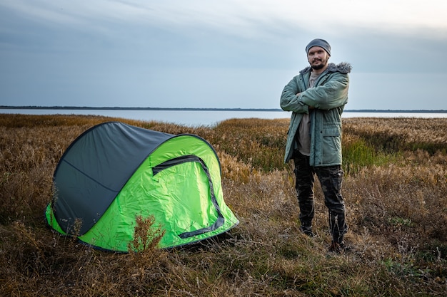 Un homme barbu près d'une tente de camping dans la nature verte et le lac. voyages, tourisme, camping.