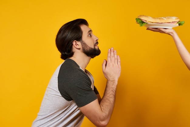 Homme barbu prie de manger un sandwich. Carnivores.