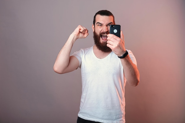 Un homme barbu puissant fait le geste du gagnant tout en tenant un téléphone