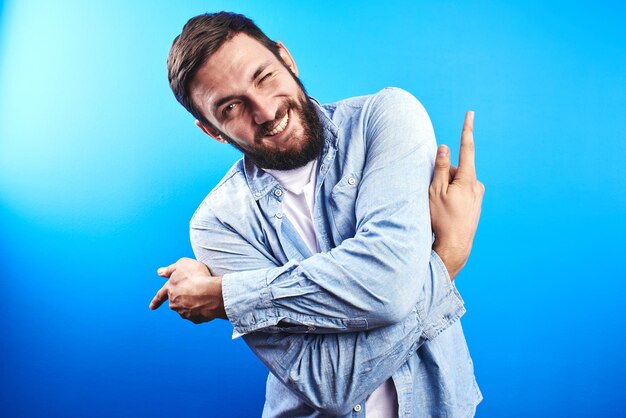 Homme barbu de race blanche dans des sourires décontractés amicaux et montre les doigts de différents côtés sur l'espace de copie sur un mur bleu isolé