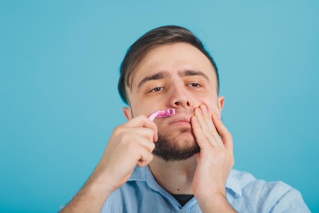 homme barbu rase un rasoir rose sur fond bleu