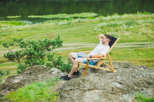 Un homme barbu s'assoit sur une chaise en bois pliable dans la nature et parle au téléphone Le concept de récréation dans la nature seule