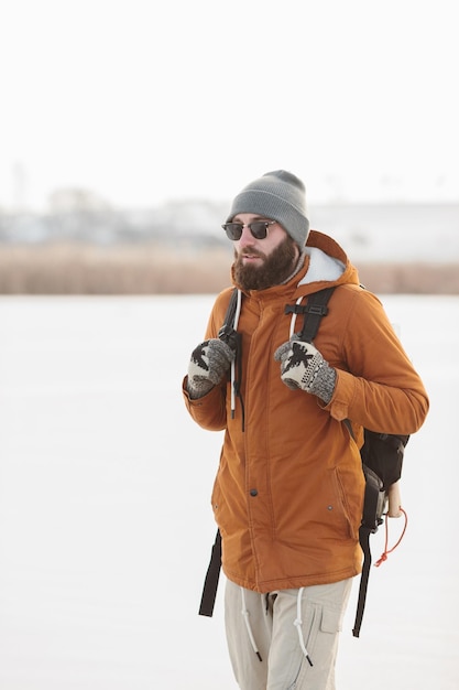 Un homme barbu avec un sac à dos dans des vêtements chauds d'hiver marche sur un lac gelé en hiver Le concept de randonnée et de mode de vie actif