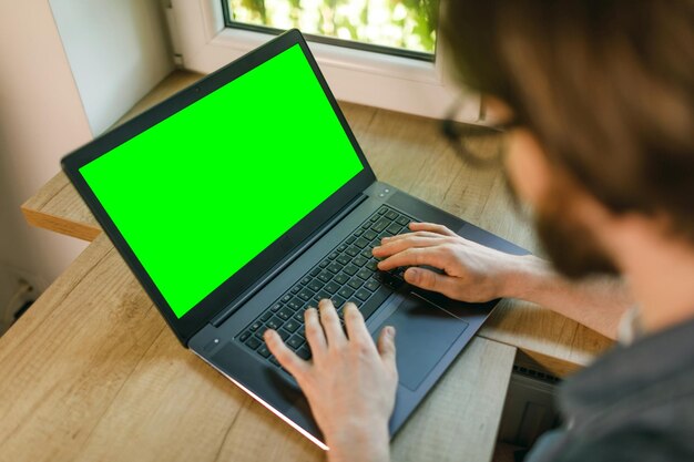 Homme barbu se reposant sur un canapé à la maison à l'aide d'un ordinateur portable à écran vert