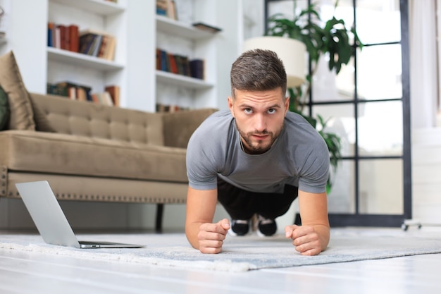 Homme barbu séduisant faisant des exercices de planche à la maison pendant la quarantaine. La forme physique est la clé de la santé