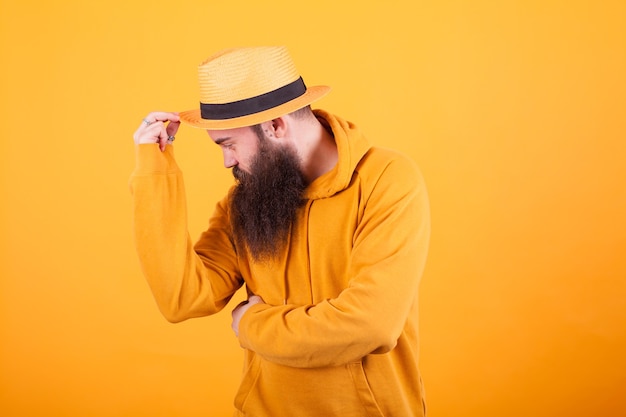 Homme barbu séduisant touchant son chapeau sur fond jaune. Chapeau sympa. Homme élégant. Barbe fraîche