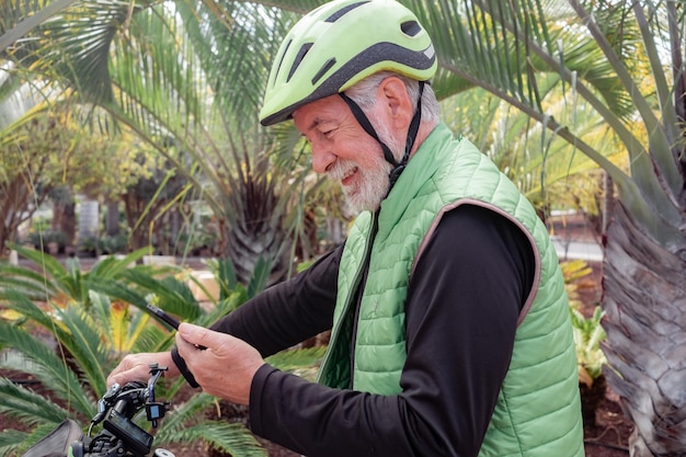 Homme barbu senior actif avec casque faisant du vélo dans un parc tropical regardant le téléphone