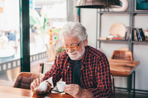 Photo un homme barbu senior souriant assis à une table de café prend son petit-déjeuner avec un café expresso et un croissant