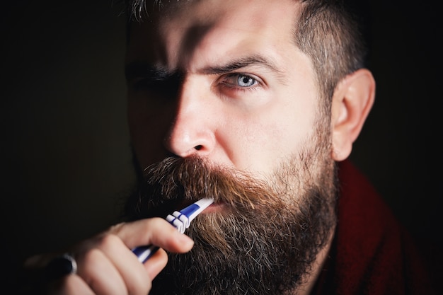 Homme barbu sérieux en T-shirt blanc se brosser les dents